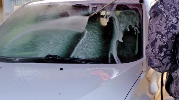 A man washes a white car at a self-service car wash with a high-pressure pistol. Washing off shampoo