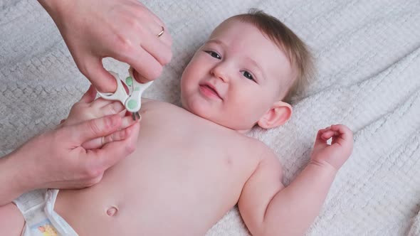 Mother trims nails on toddler baby boy hand with small scissors, a...