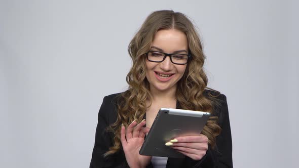 Pensive Businesswoman Texting on Her Tablet with Smile on Gray Background in Studio