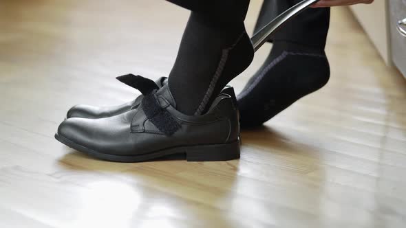 Boy is putting on new black shoes with the help of special object indoors. 