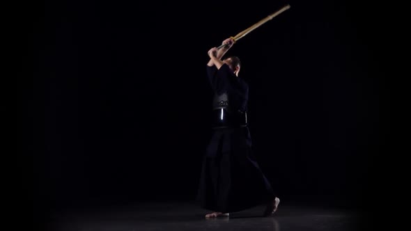 Masculine Kendo Warrior Practicing Martial Art with the Bamboo Bokken on Black Background. Slow