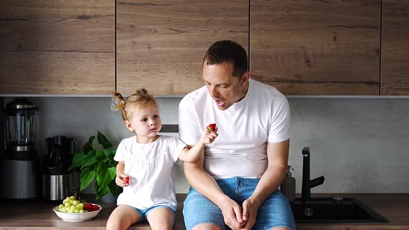 Cute Little Girl and Her Handsome Dad are Eating Fruit in Modern Kitchen