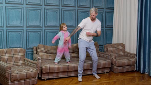 Young Father Babysiter and Little Kid Daughter Jumping Dancing on Sofa in Modern House Living Room
