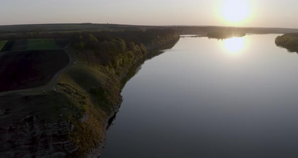 view from a drone to a large river at sunset, the sun is surrounded by forests and green fields
