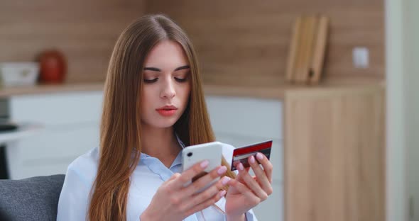 Young Woman Is Sitting on the Sofa in the Living Room and Pays for Purchases Online Using a