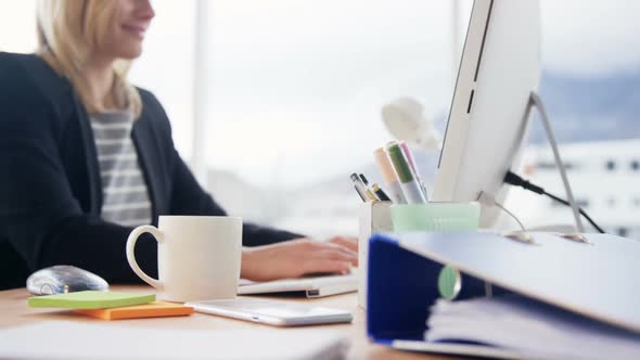 Businesswoman drinking cup of coffee while working on computer