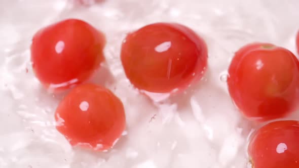 Slow motion of small tomatoes falling into a container with water for cleaning.