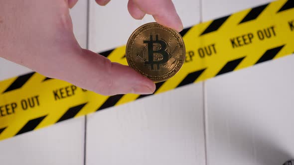A Bitcoin Coin Lying on a Yellow Warning Tape with the Inscription KEEP OUT