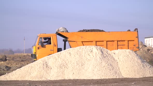 Big Yellow Dump Truck Loaded with Dirt is Driving Through Construction Site