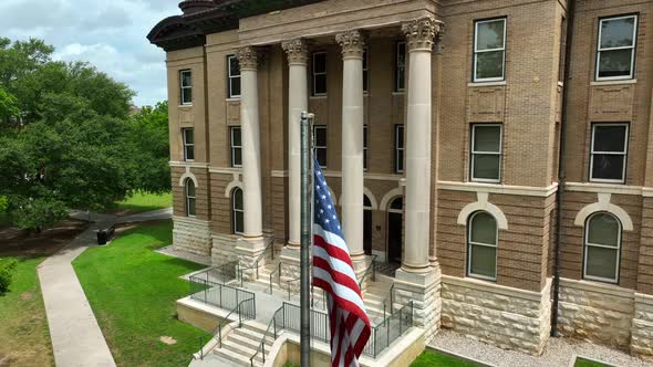 Old brick courthouse building with USA flag. San Marcos Texas. Rising aerial.