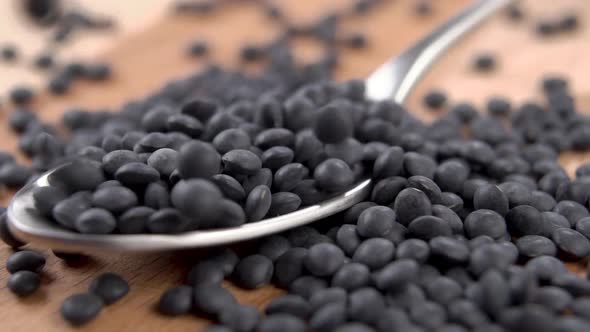 Black bean lentils fall into a full metal spoon on a board in slow motion