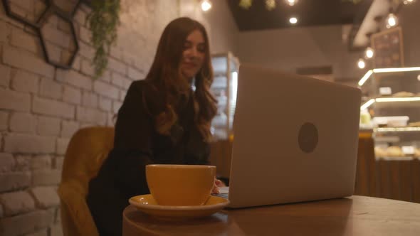 A Beautiful Young Girl with a Sweet Smile Sits in a Cafe with Original Interior and Works at a