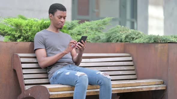 Young African Man Using Smartphone on Bench 