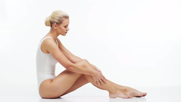 Young, beautiful, fit and natural blond woman in white swimsuit applying skincare cream.