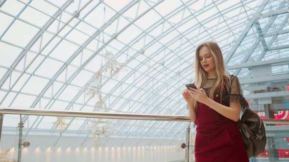 Happy Teenage Girl Holding Bags with Purchases, Smiling While Looking at Phone in Shopping Center