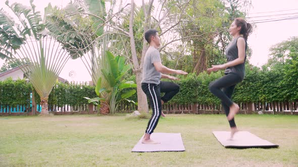 Fit happy people working out outdoor. Asian couple exercising together on a yoga mat at home garden