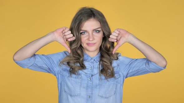 Young Girl Gesturing Thumbs Down Isolated on Yellow Background