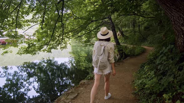 A young girl in a hat walking along the path along the lake. Plitvice Lakes