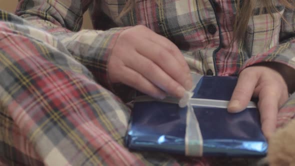 Woman in pajamas opening gift wrapped in paper close up