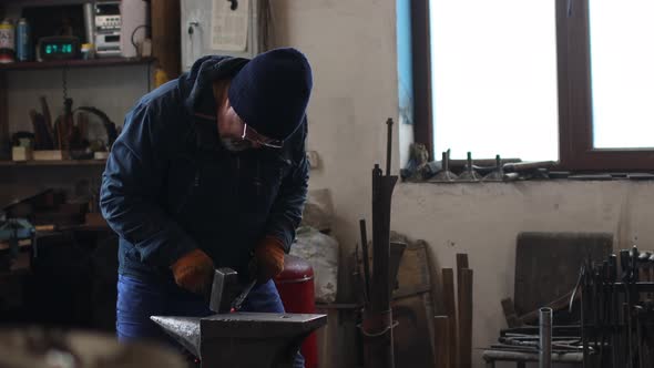 Blacksmith Forges and Makes Metal Detail with Hammer and Anvil at Forge