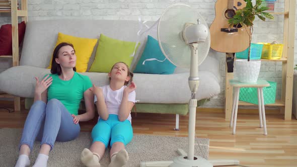 Mother and Daughter Next To the Fan Suffers From Hot Weather