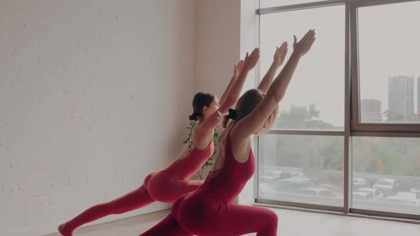 Two Women in Red Sports Uniforms Make Virabhadrasana in Yoga Studio