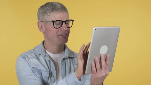 Casual Senior Man Browsing Internet on Tablet, Yellow Background