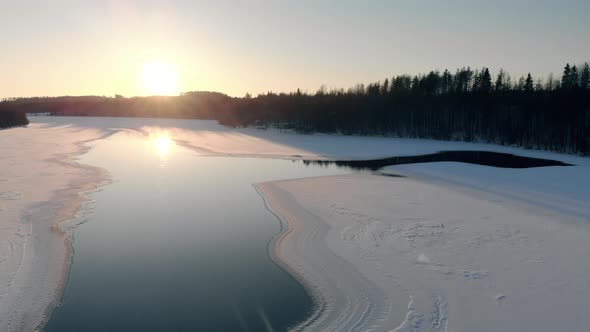 Frozen river in the middle of a forest in an aerial view at sunrise