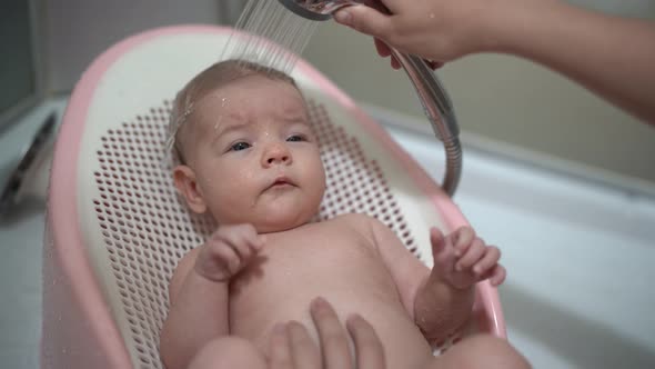 Newborn Lies on a Slide in the Bathroom and His Mother Washes His Head From the Shower