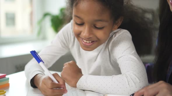 Adult Mixed Race Woman Teacher Sitting and Talking To American Black Student Child in School Class