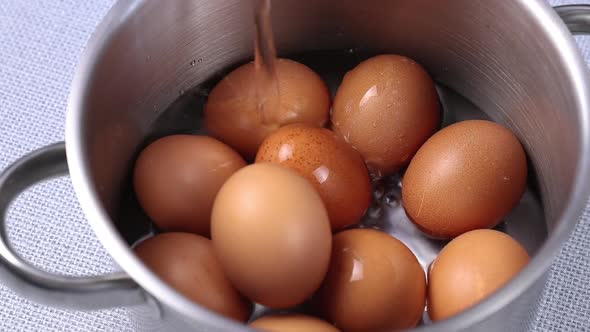 pour water in a metal pan with yellow eggs close-up before boiling