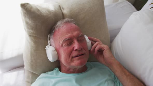 Caucasian senior man wearing headphones singing while lying on the couch at home