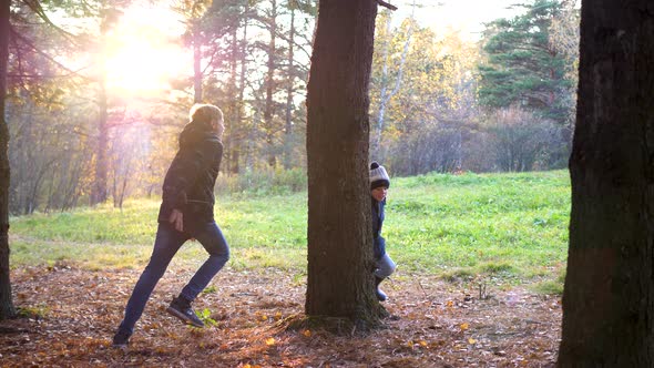 A Teenager Plays with a Child, Runs in the Park Around a Tree and Catches Up with Him. The Sun's