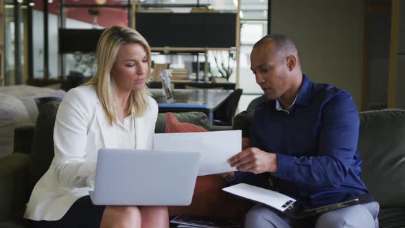 Two diverse business colleagues using laptop and discussing paperwork in a casual meeting