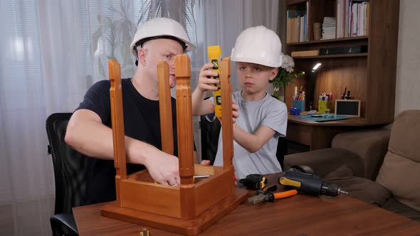 A Little Boy with His Father in White Helmets Fixing a Wooden Chair Together