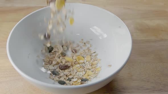 Slow Motion Slider Shot of Pouring Muesli into a White Cereal Bowl on a Kitchen Counter for Breakfas