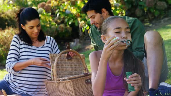 Girl blowing bubble while her parents sitting in background 4k