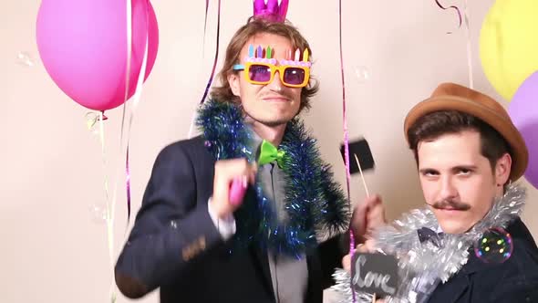 Two men holding sign in love and dancing in photo booth