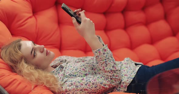 Woman Using Smartphone Sitting on Orange Sofa