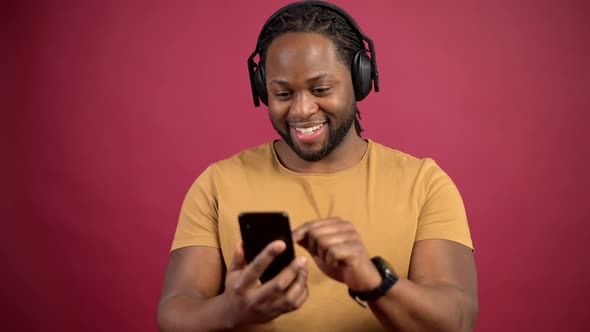 Cheerful AfricanAmerican Guy Listens Music Isolated on Red Background