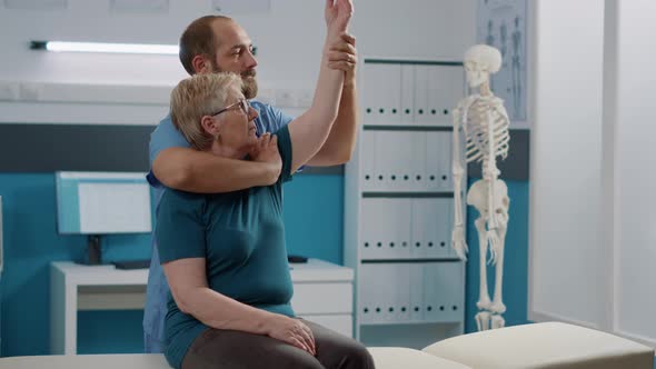 Male Osteopath Assisting Senior Woman to Stretch Arms Muscles
