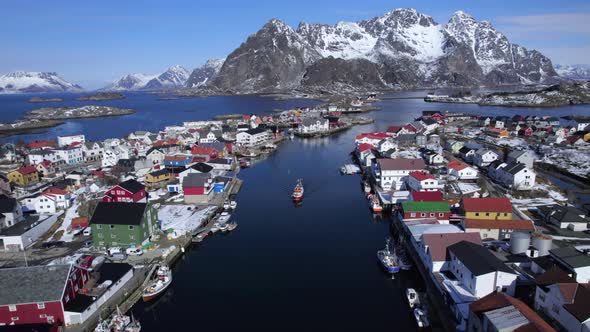 Henningsvaer Harbor on a calm sunny day with blue sky and reflecting water, Backward aerial shot, Lo