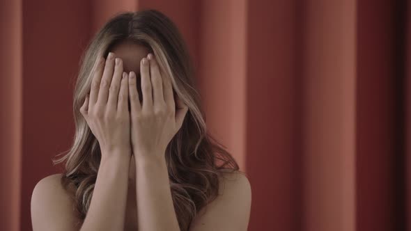 Blonde Woman Opens Her Face with Hands Looks at the Camera in Pink Studio