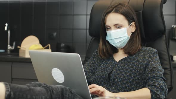 Woman using protective medical face mask while working on laptop at home. Work from home