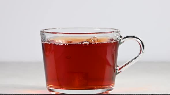 Throwing brown sugar cubes in glass cup full of black tea over white background