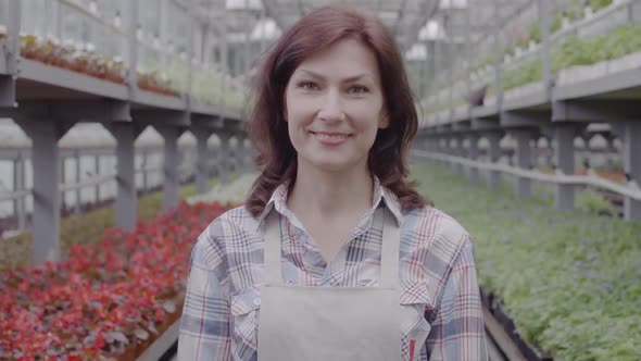 Portrait of Happy Caucasian Woman Advertising Bottle of Pesticides in Greenhouse. Positive Beautiful