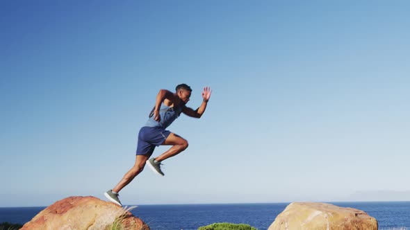 African american man exercising outdoors jumping on rocks in countryside on a mountain