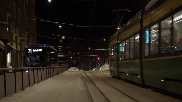 Metro trains and buses transit snowy winter street at night, Helsinki