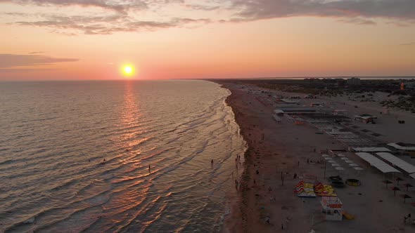 Aerial View of Beautiful Sunset Over Sea and Sand Beach, People Are Swimming in the Waves.