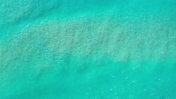 A beautiful above shot of clear aquamarine water in the ocean with a wave passing by and leaving sea